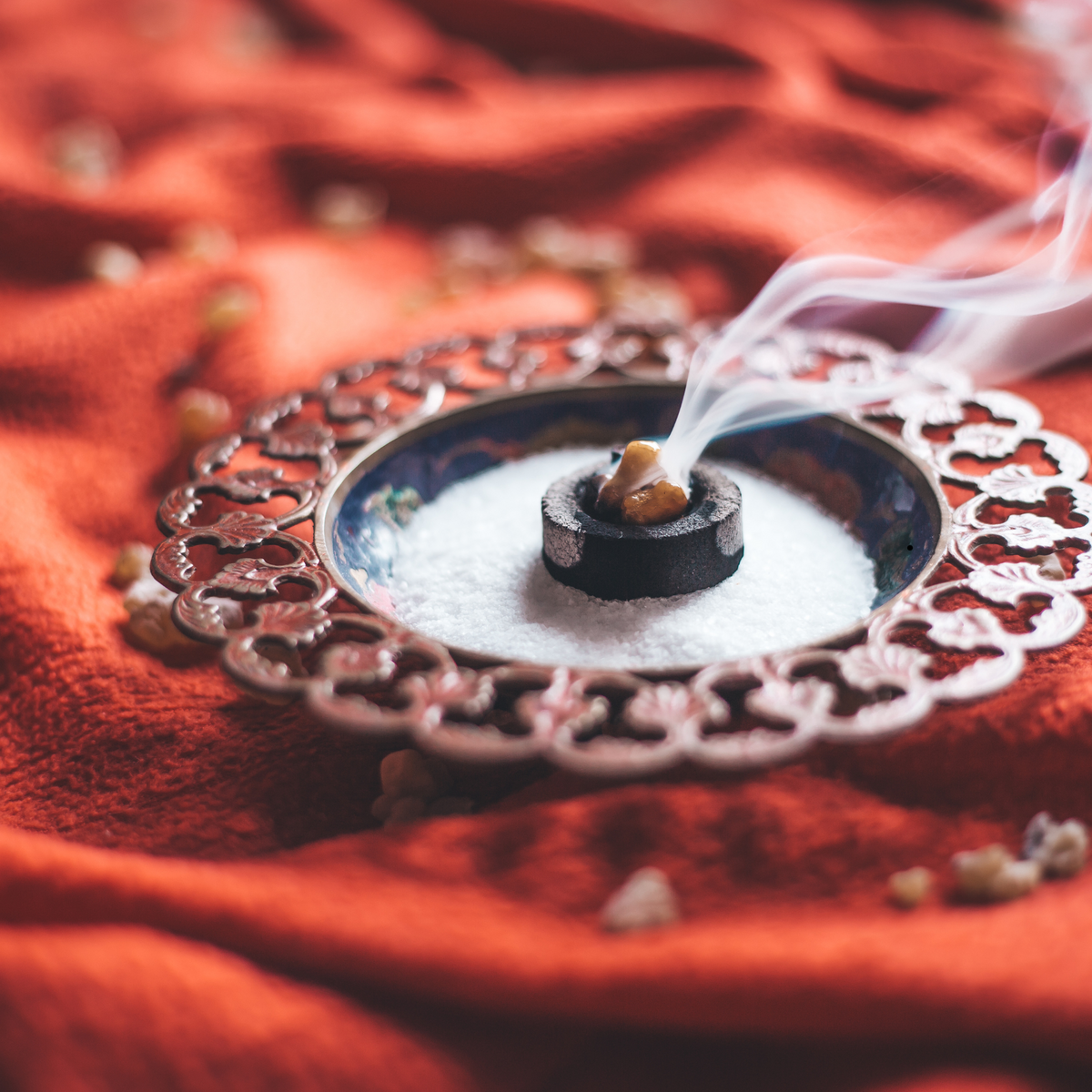 Frankincense resin smoking on a charcoal disc in an ornate metal dish.