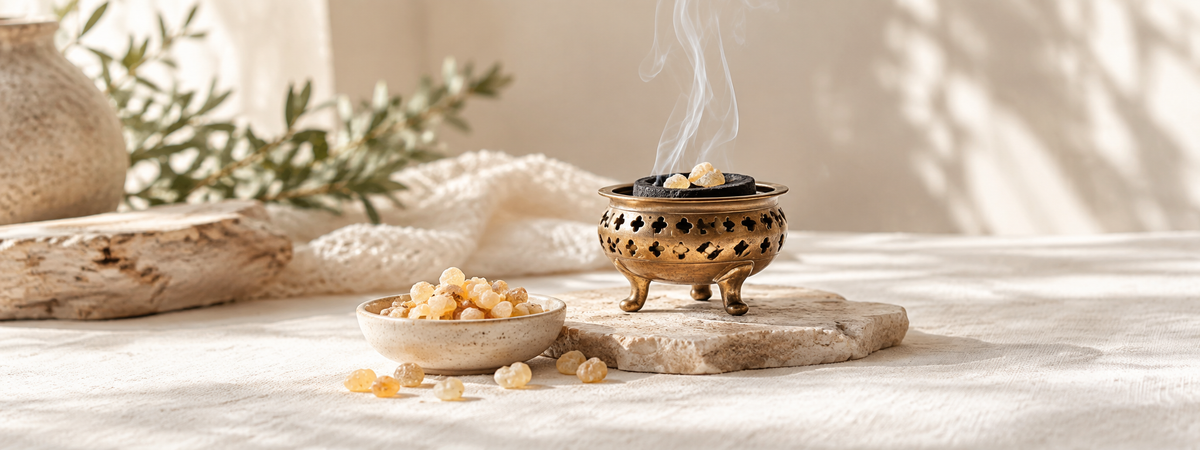 A restrained frankincense ritual: a few pale golden resin tears in a small plain ceramic dish beside a brass incense burner on heat-resistant stone.