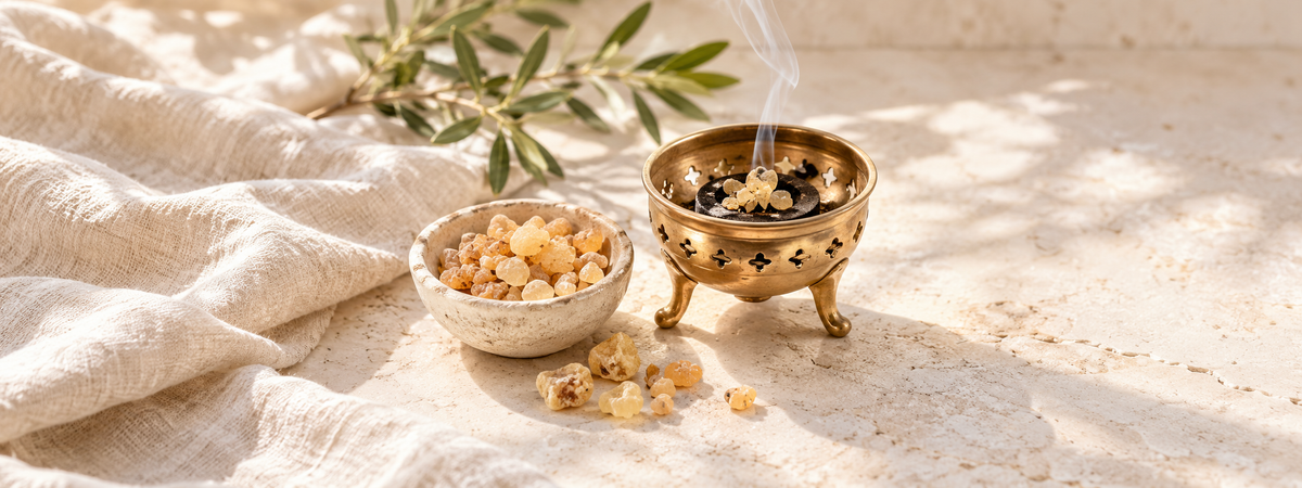 Golden frankincense resin tears in a small plain stone bowl beside an unbranded brass burner on heat-resistant pale stone.