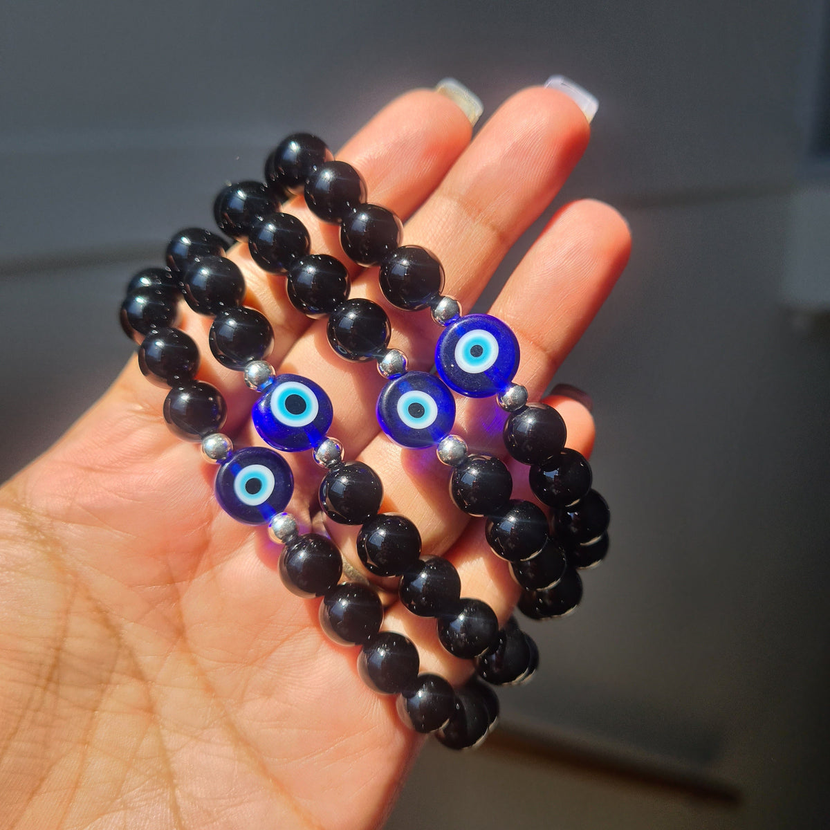Hand holding black bead bracelets with blue evil eye charms.