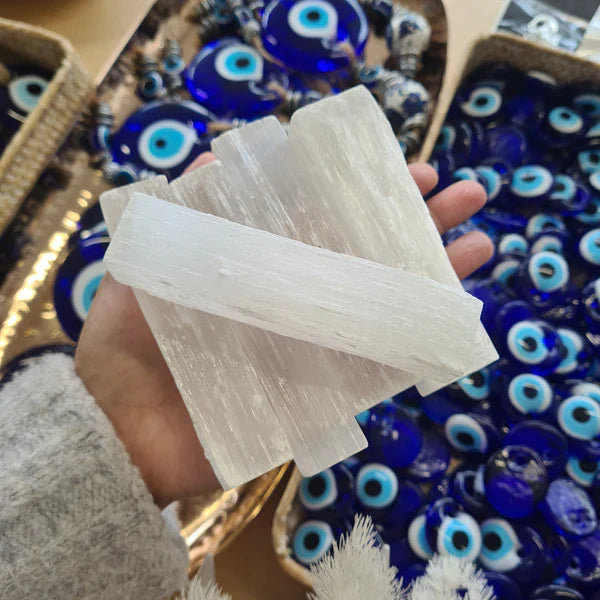 Hand holding white selenite pieces above blue evil eye beads.