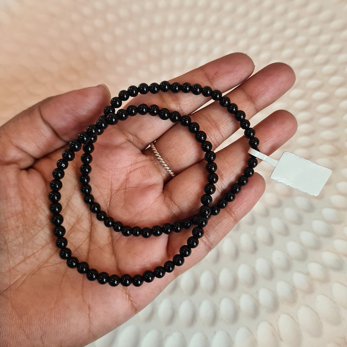 Hand holding black beaded bracelets with a white crystal point in the background.