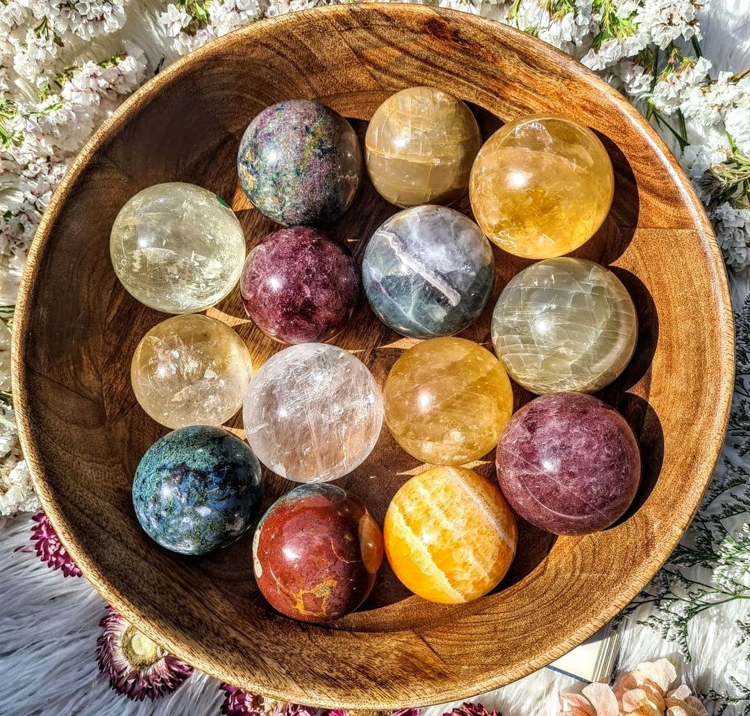 Colourful polished crystal spheres arranged inside a round wooden bowl.