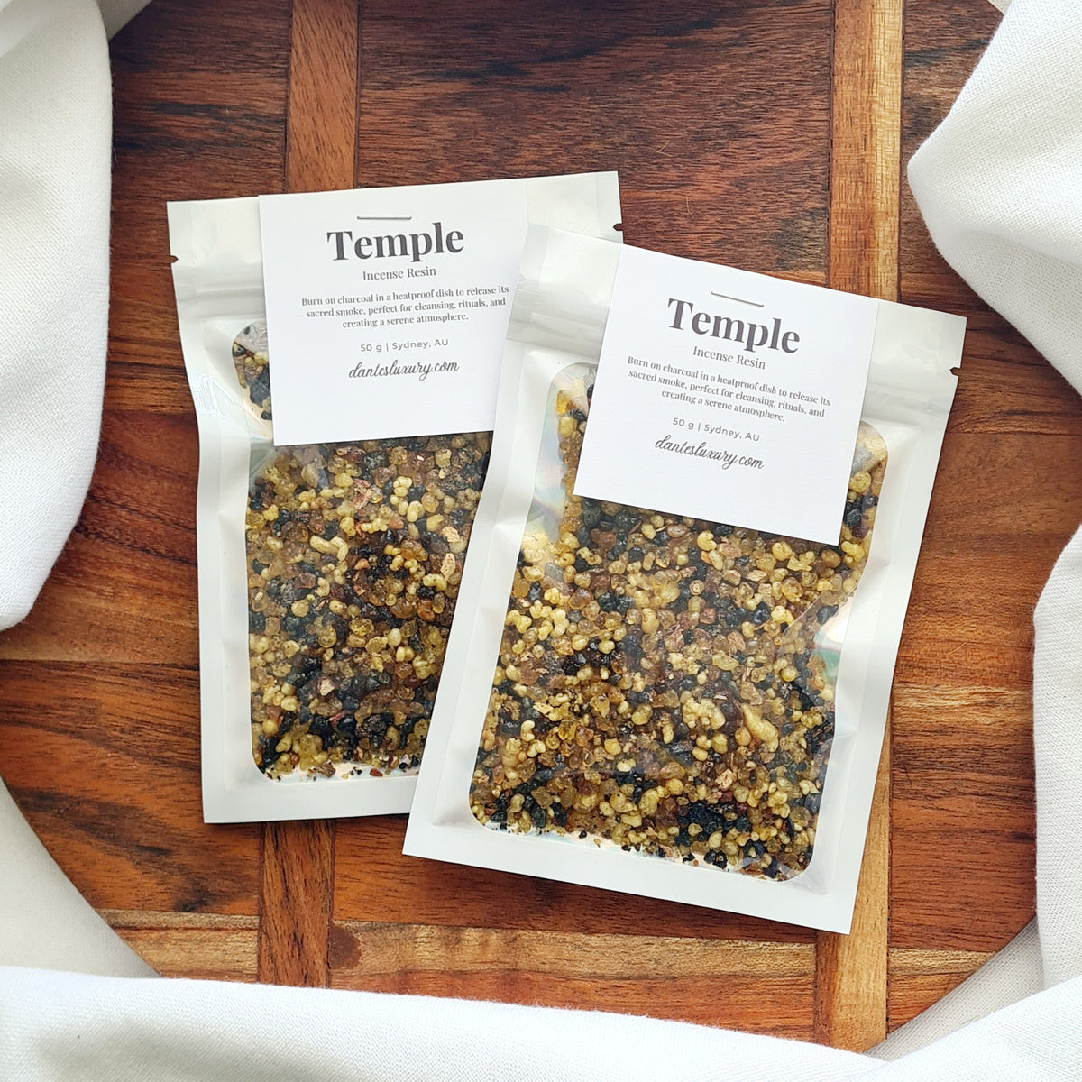 Two clear packets of Temple resin incense on a wooden tray.