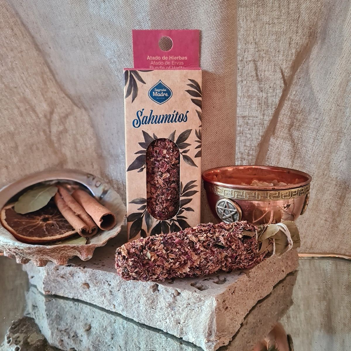 Botanical incense bundle and illustrated packet beside a brass-coloured bowl on a stone block.