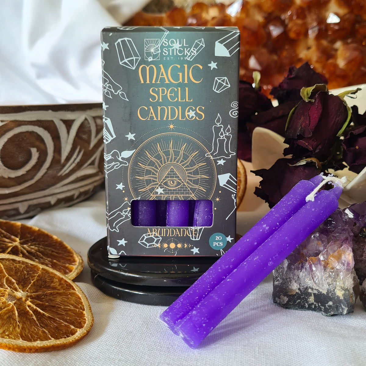 Purple spell candles beside their illustrated packaging, crystals and dried orange slices.