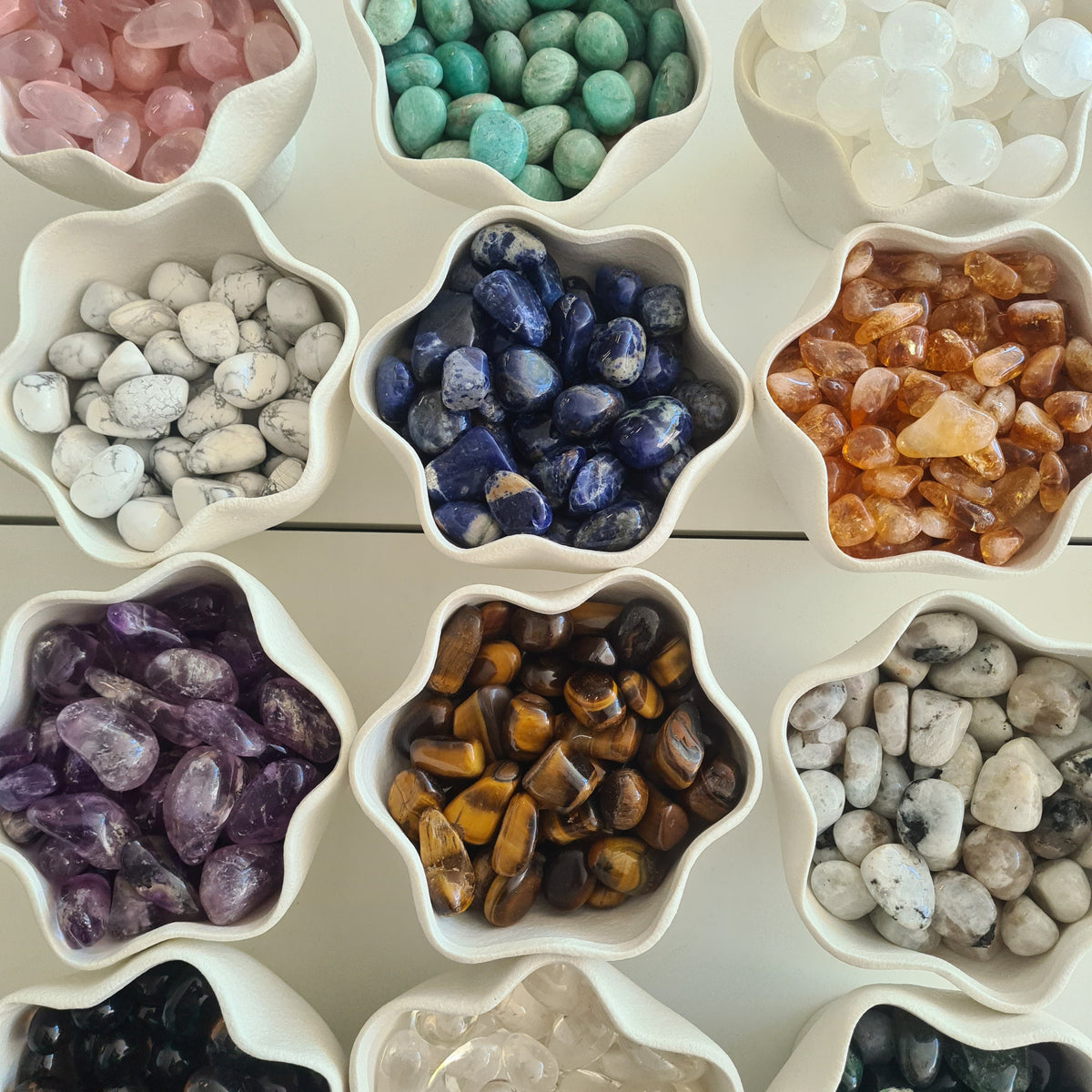 Assorted tumbled crystals sorted by colour into white star-shaped bowls.