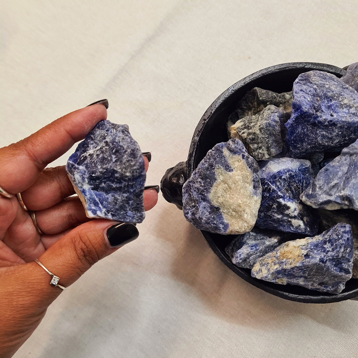 Hand holding a rough blue stone above a bowl of blue and pale raw crystals.