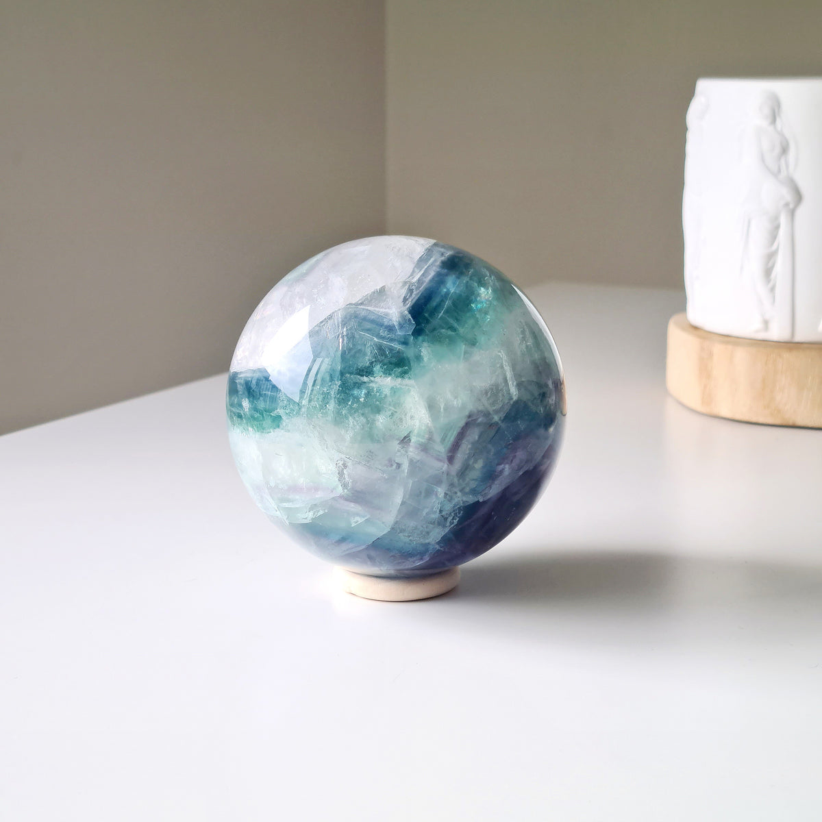 Rainbow Fluorite sphere, 8.5 cm, with green, blue and purple layers and natural internal formations, displayed on a shelf.