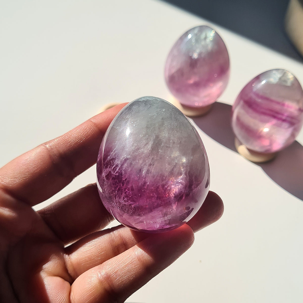 Gemmy Fluorite egg held in a hand, showing pink and purple bands.