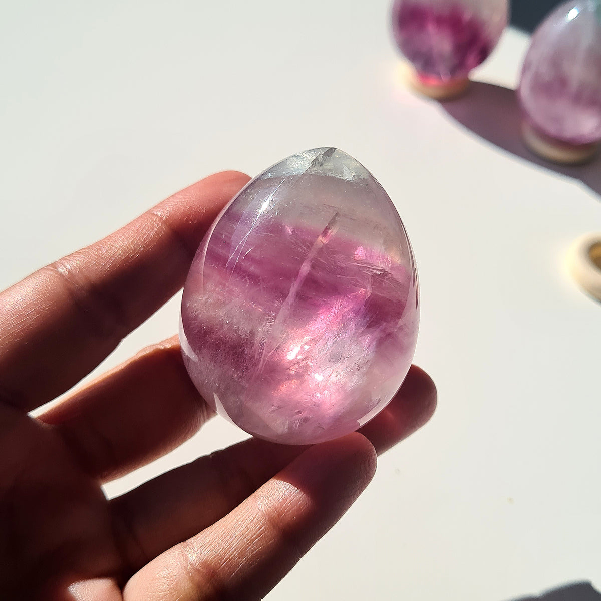 Gemmy Fluorite egg with pink and purple layers held in sunlight.