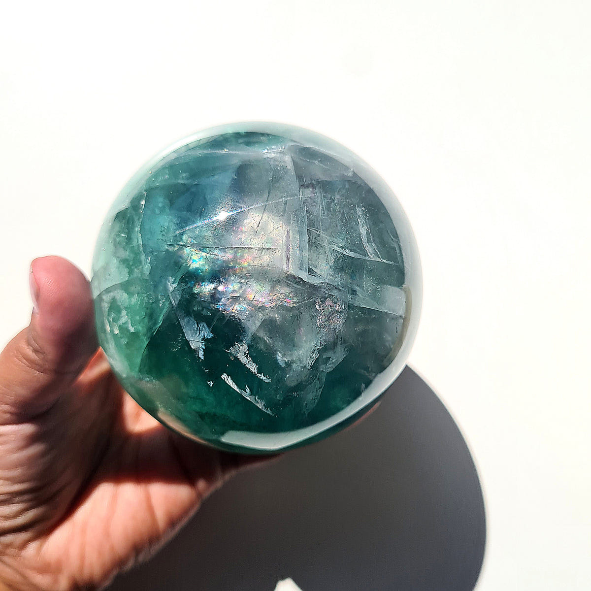 Green Fluorite sphere, 8.4 cm, with translucent teal tones and natural internal formations, held in a hand.