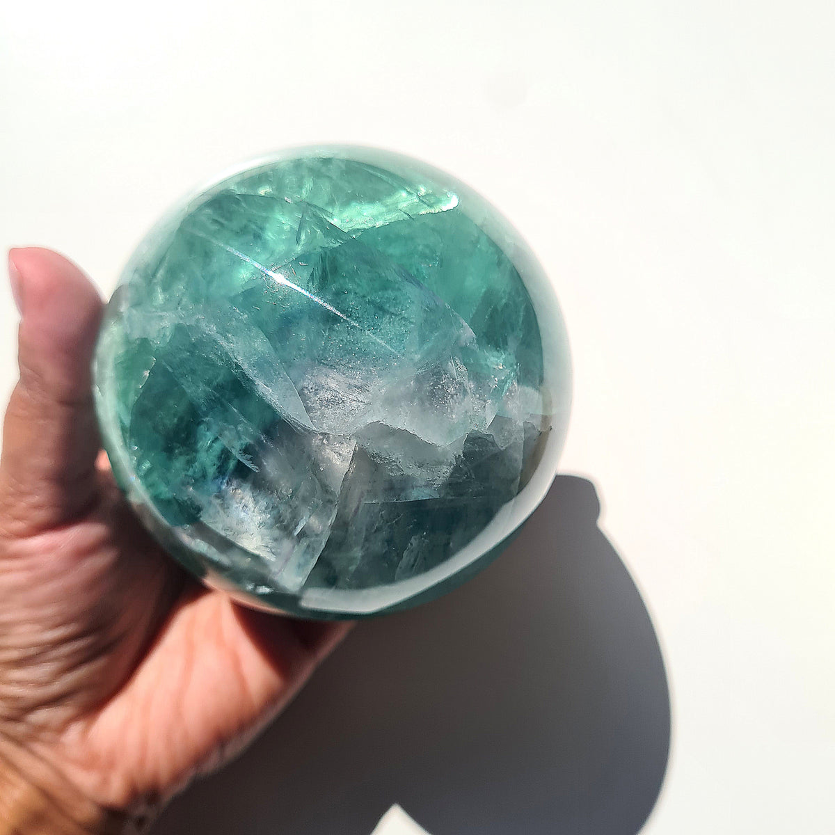 Green Fluorite sphere, 8.4 cm, with translucent teal tones and natural internal formations, held in a hand.