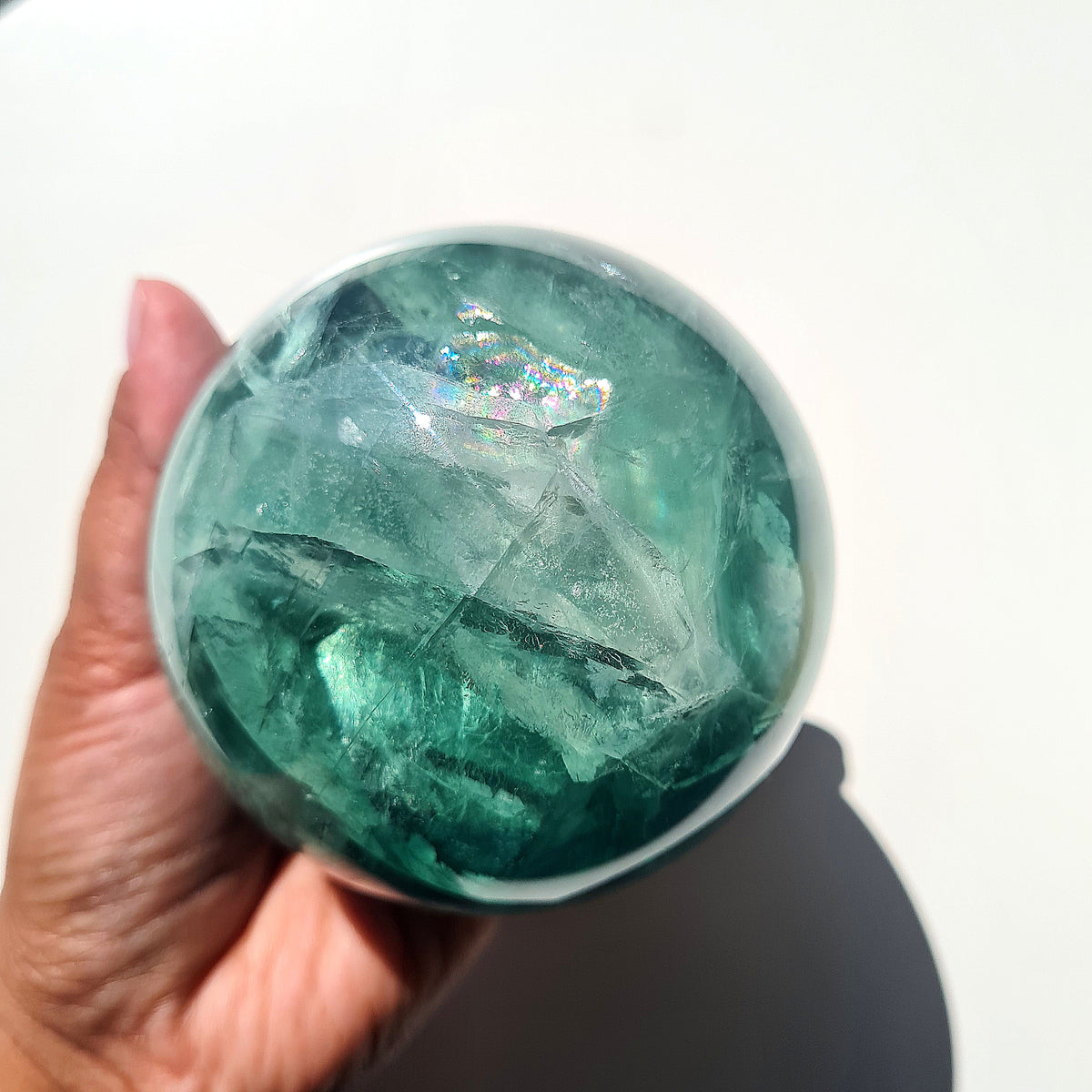 Green Fluorite sphere, 8.4 cm, with translucent teal tones and natural internal formations, held in a hand.