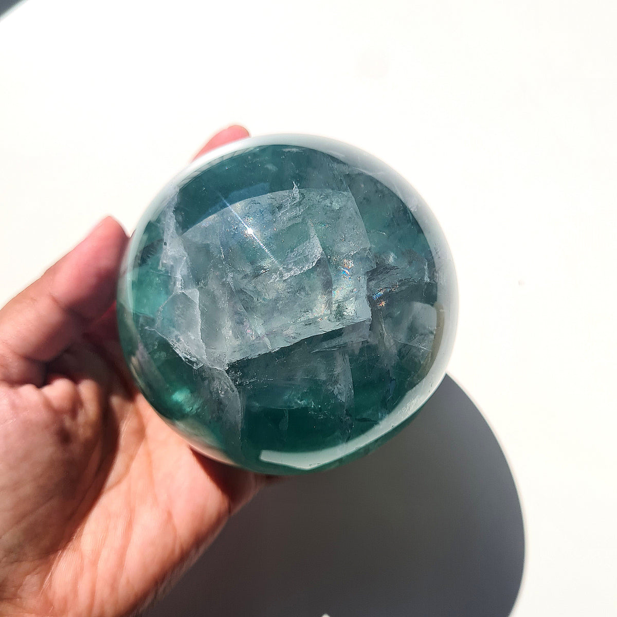 Green Fluorite sphere, 8.4 cm, with translucent teal tones and natural internal formations, held in a hand.