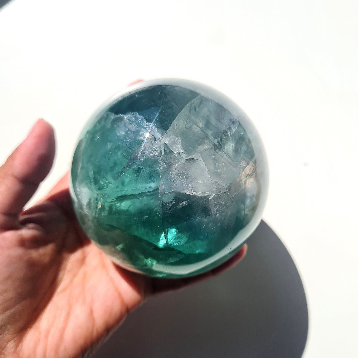 Green Fluorite sphere, 8.4 cm, with translucent teal tones and natural internal formations, held in a hand.