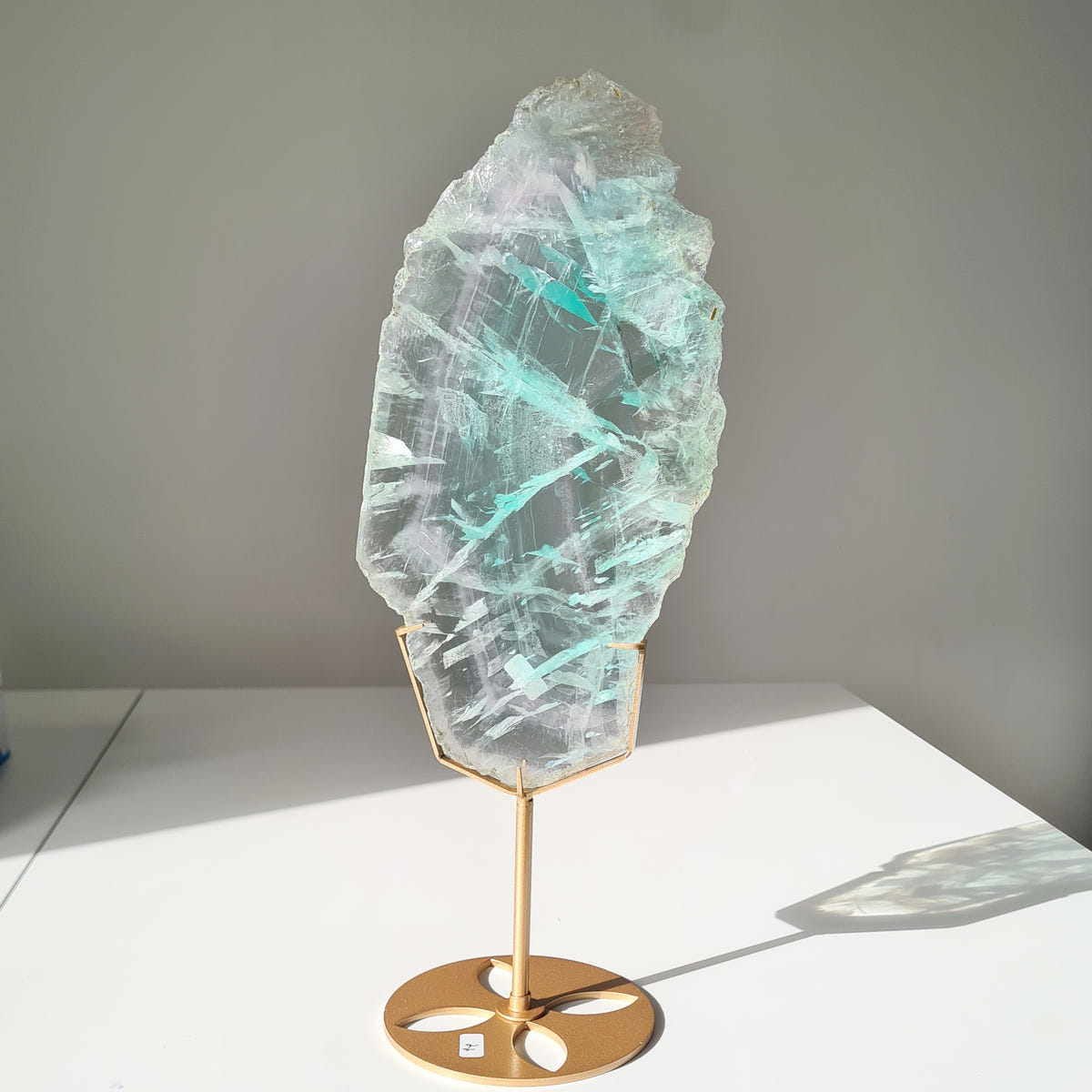 Tall fluorite Dream Portal slab with turquoise bands and a rough upper edge on a gold-coloured stand.