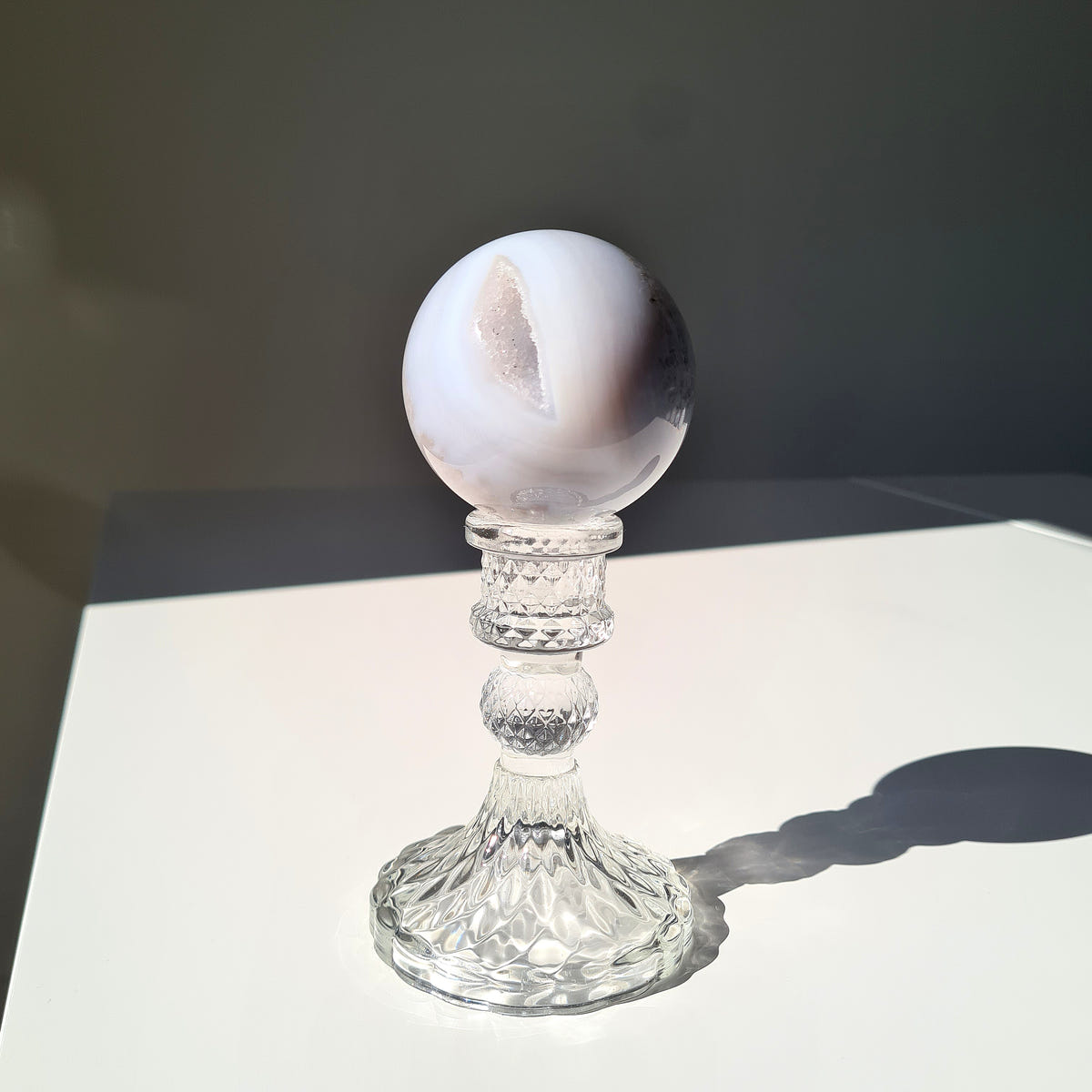 White and grey Agate sphere with a narrow crystal-lined opening on a clear pedestal.