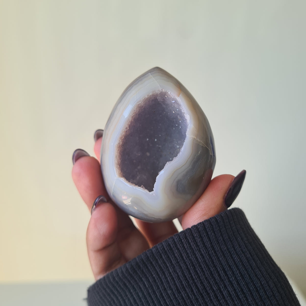 Agate geode egg with a pale grey border around a dark crystal pocket.
