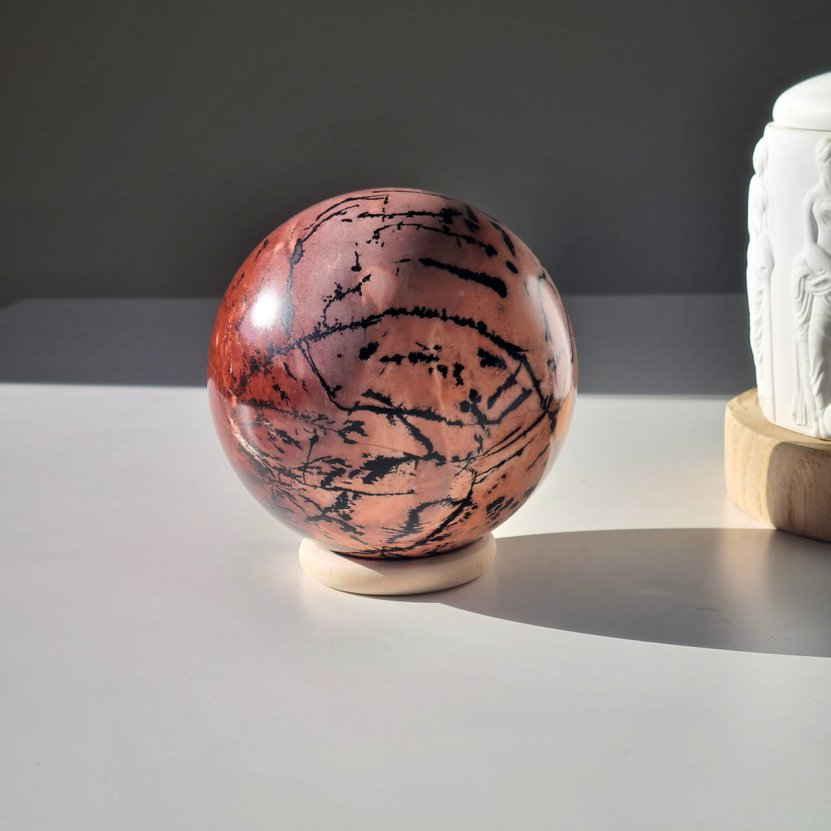Polished picture jasper sphere on a ring stand, with broad black lines across a terracotta surface.