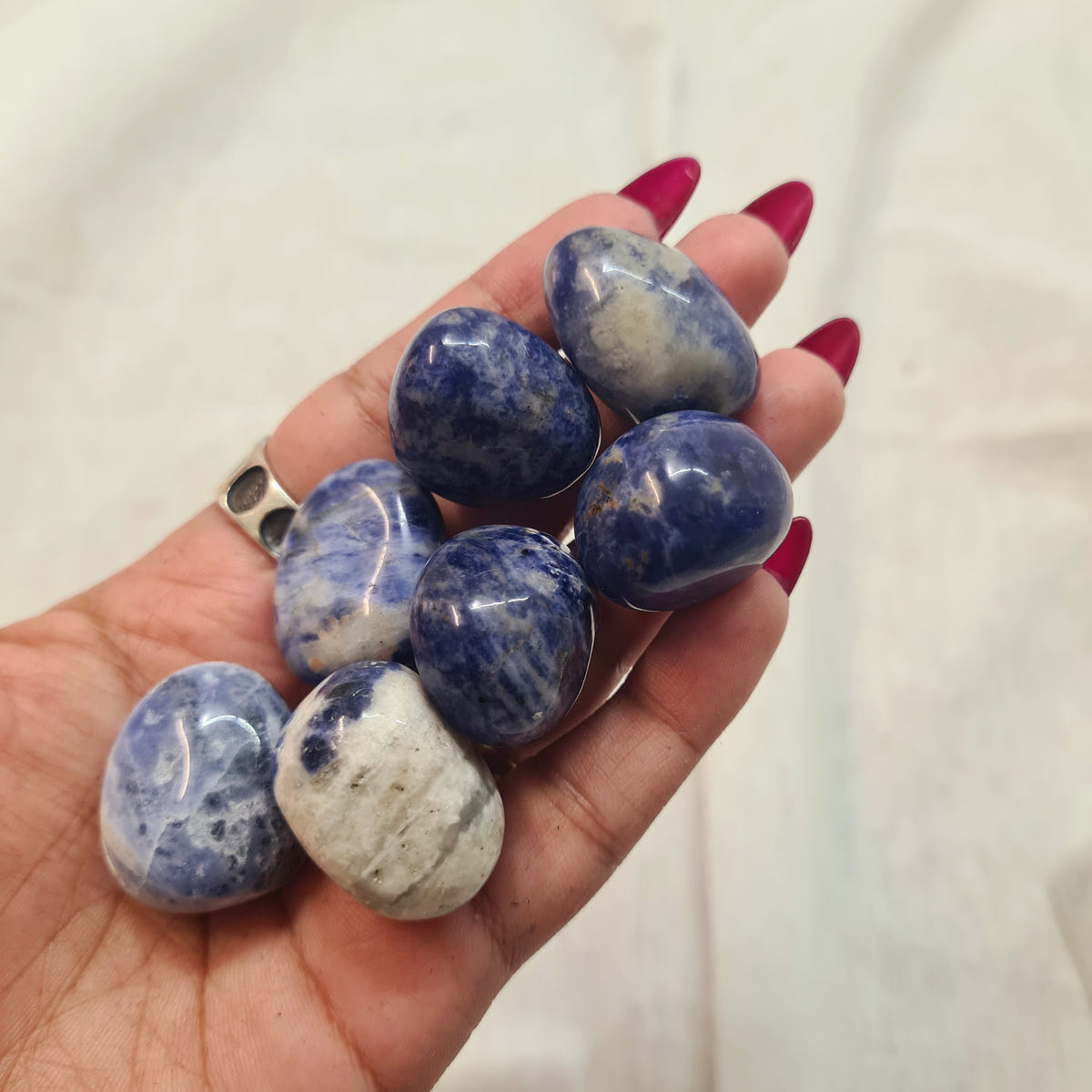 Hand holding smooth sodalite tumbles with deep blue, white and cream mineral patterns.