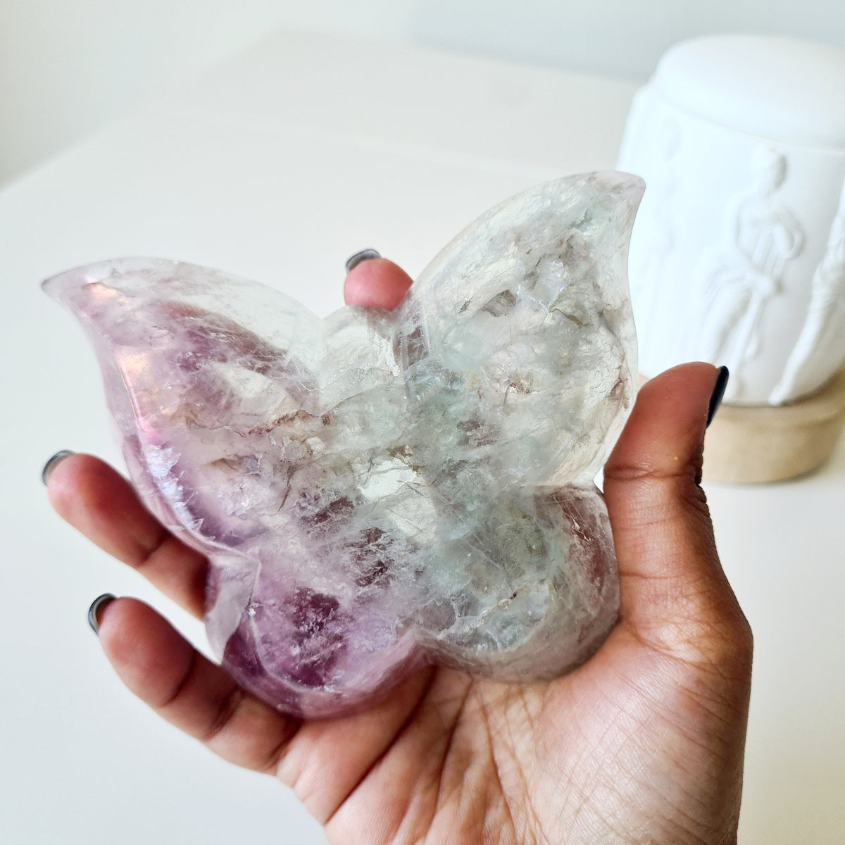 Hand holding a fluorite butterfly bowl with pale mint-green and purple wing patterns.
