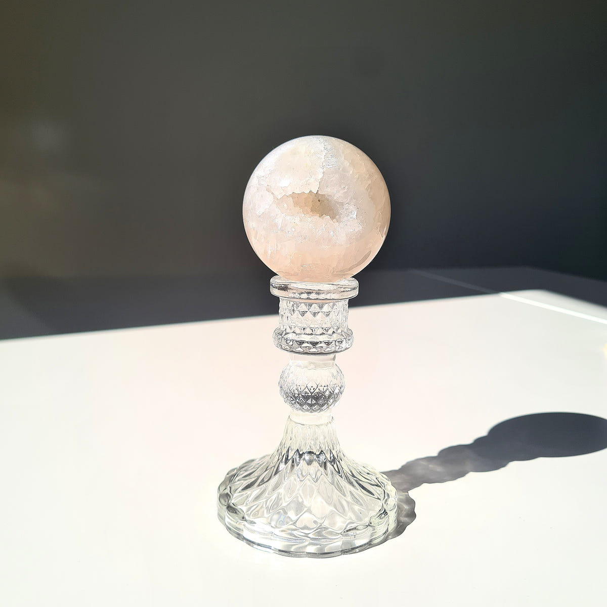 Pale peach Agate geode sphere with broad crystalline detail across the front on a clear pedestal.