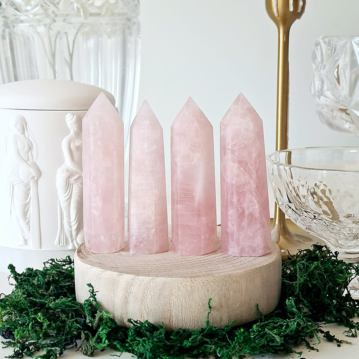 Four pale pink rose quartz crystal points displayed in a row on a round wooden base.