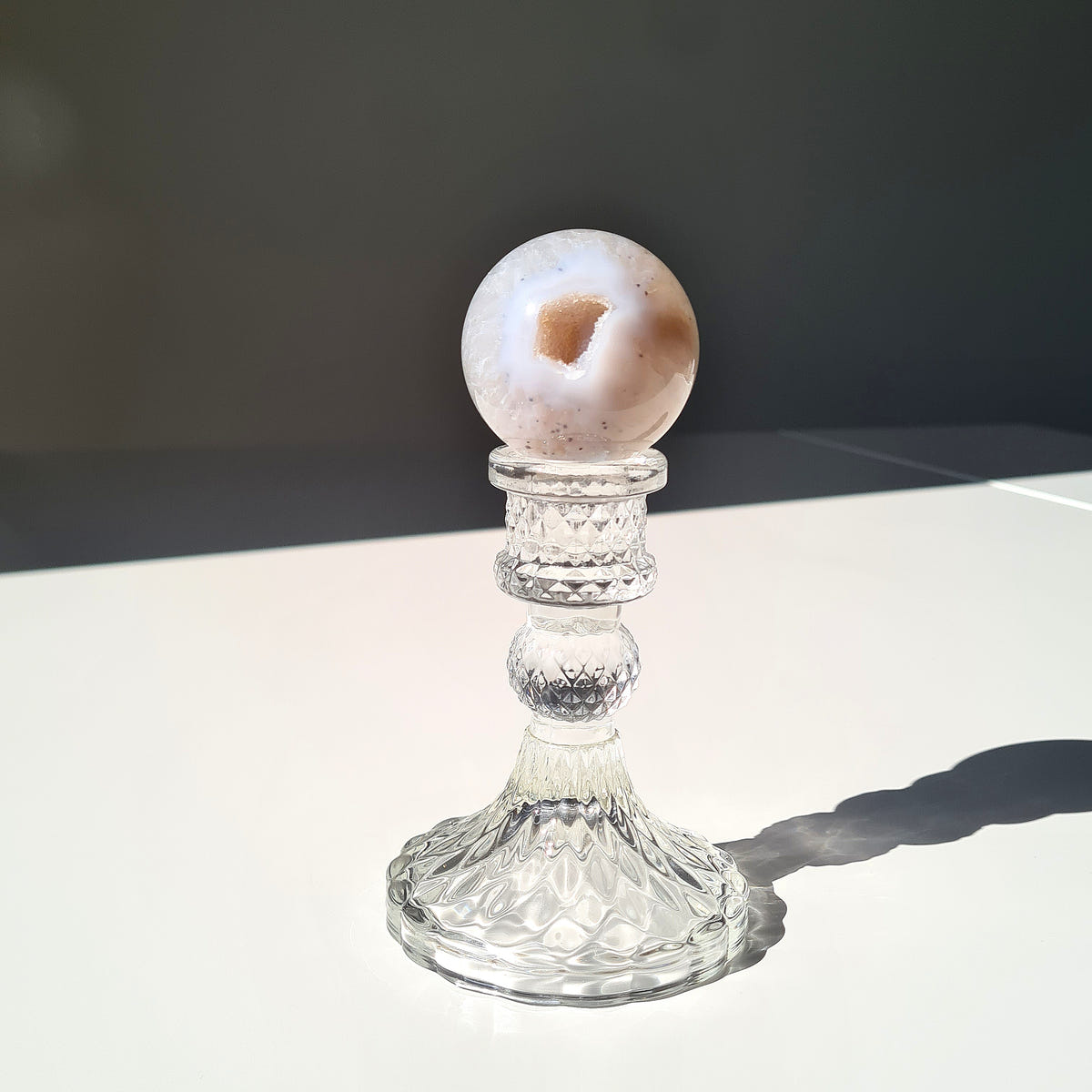 White Agate geode sphere with a small crystal pocket on a clear pedestal.