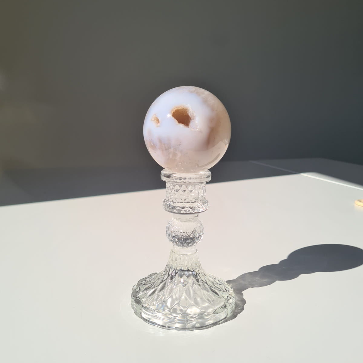 Pale Agate geode sphere with a warm-toned crystal pocket on a clear pedestal.