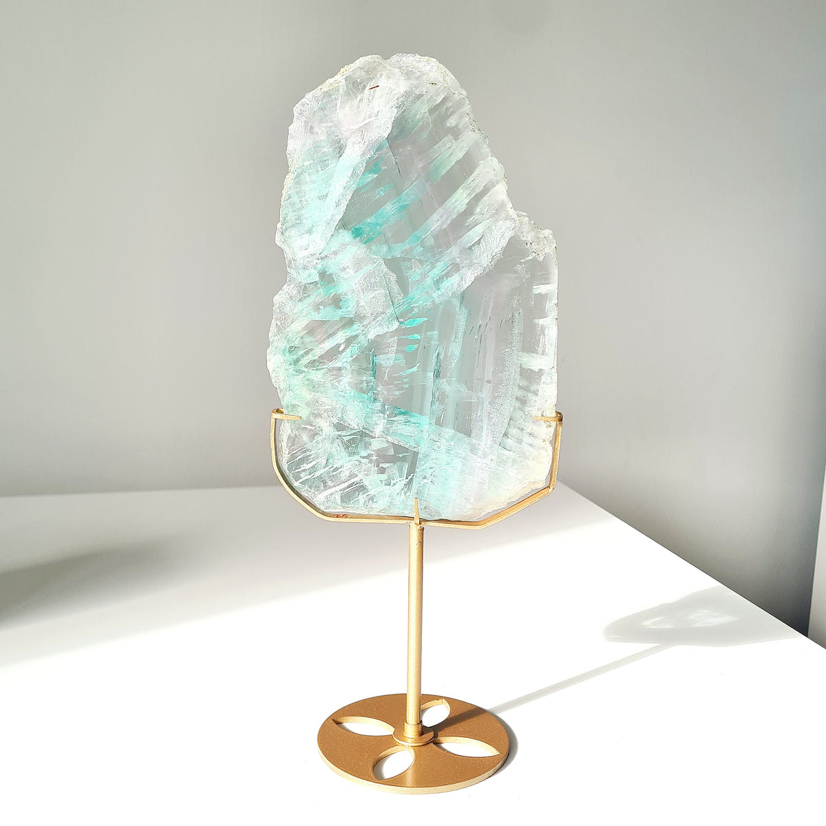 Pale aqua Fluorite slab with diagonal bands displayed on a gold-coloured stand.