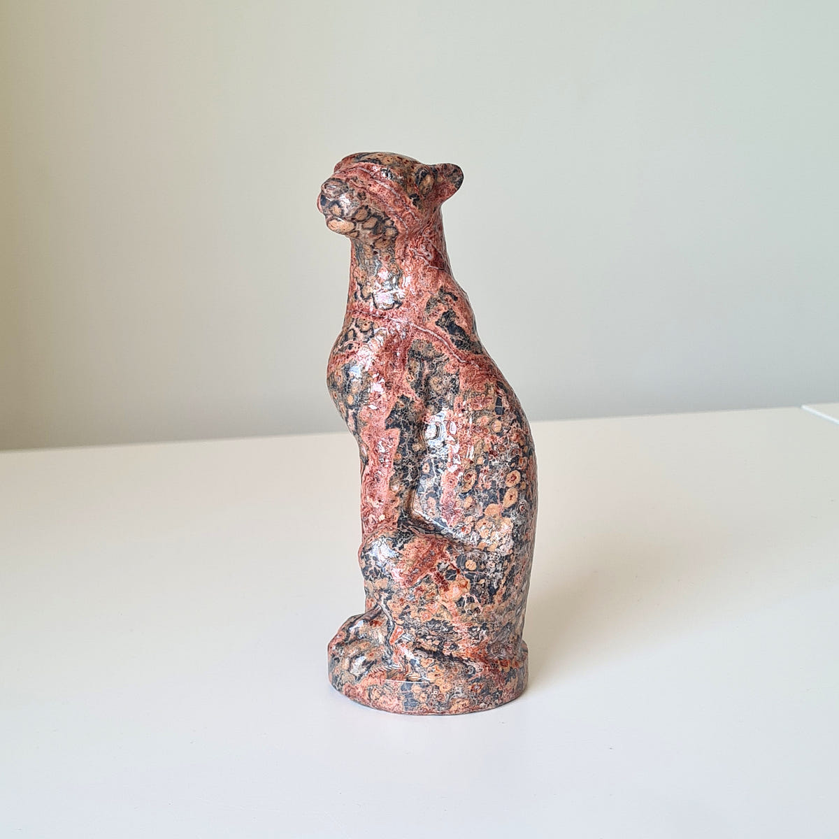Jasper leopard carving B with red, pink and black mottling, seated upright on an oval base.