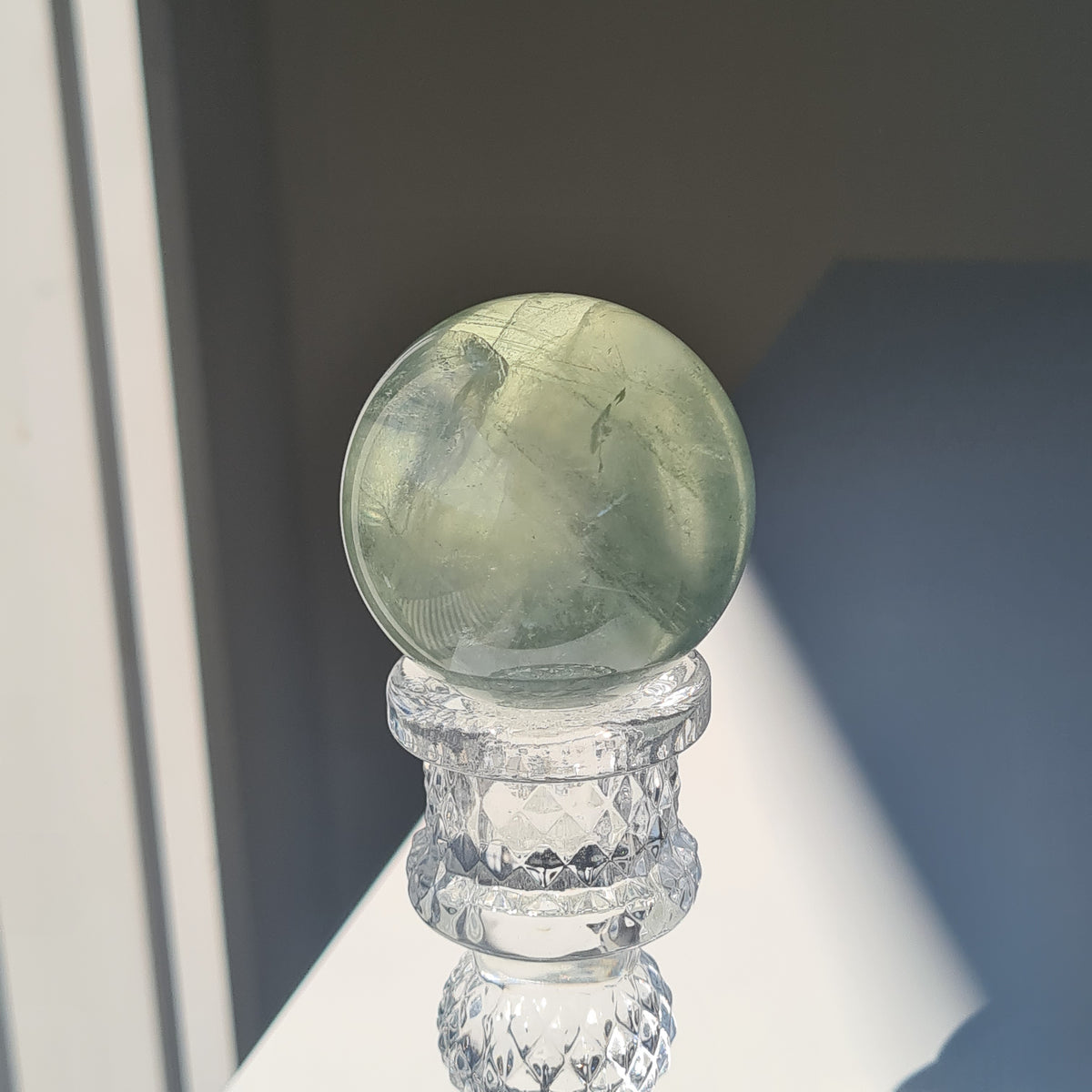 Close view of a pale green fluorite sphere with translucent bands on a clear stand.