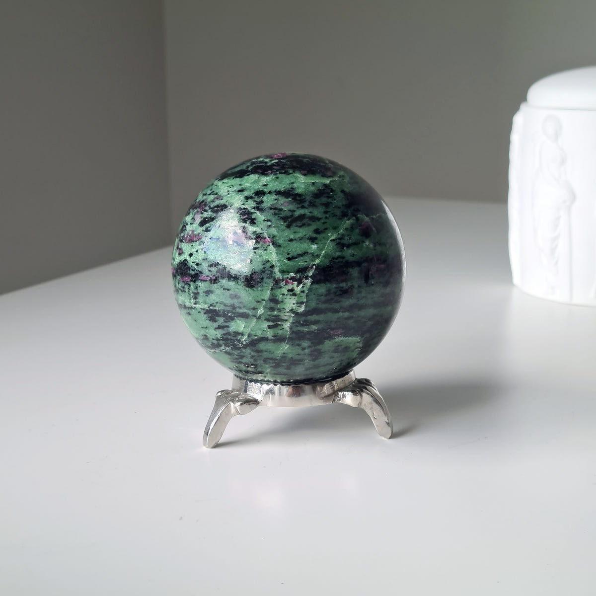 Ruby in zoisite sphere with green, black and small pink mineral patterns on a silver-coloured stand.