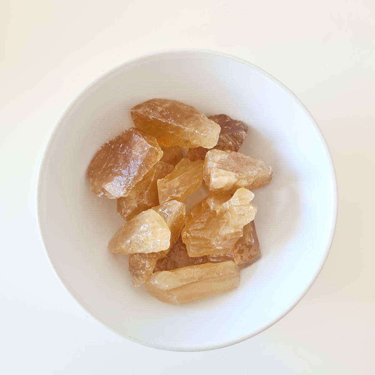 Small rough honey calcite pieces in translucent golden-yellow tones arranged in a white bowl.
