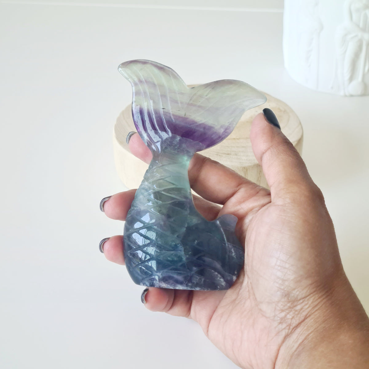 Hand holding a fluorite mermaid tail carving with purple bands and a blue-green base.