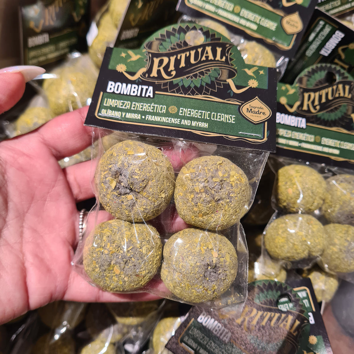 Hand holding a clear Ritual Bombita packet with four round botanical incense pieces and a green label.