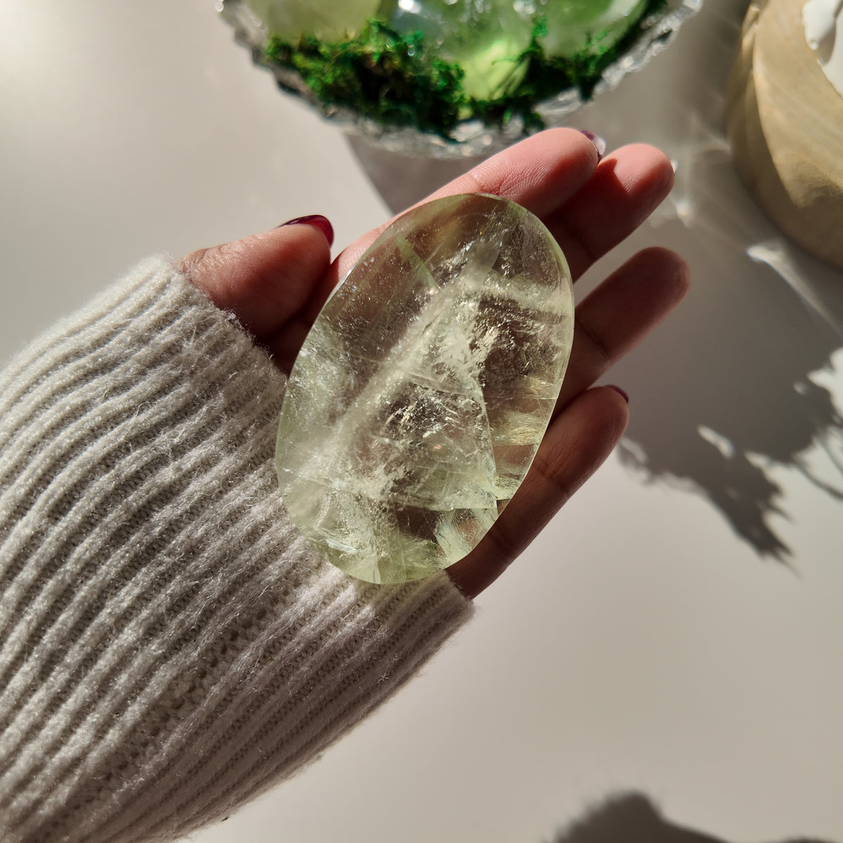 Hand holding polished pale-green Fluorite pocket stone A, with translucent areas and internal veils.