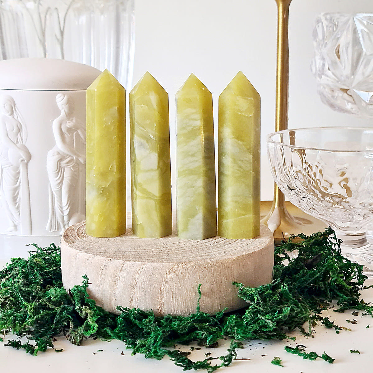 Five yellow-green jade crystal points displayed together on a round wooden base.