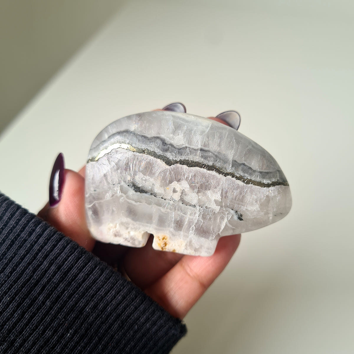Hand holding a quartz and pyrite Zuni bear carving with pale grey and white bands and a dark horizontal seam.