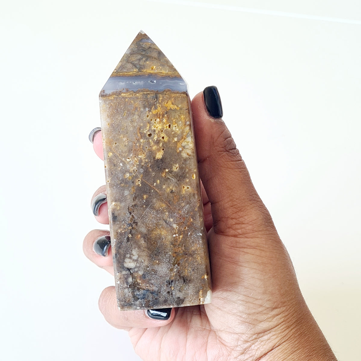 Polished back of a hand-held agate tower showing golden-brown patches and grey stone.