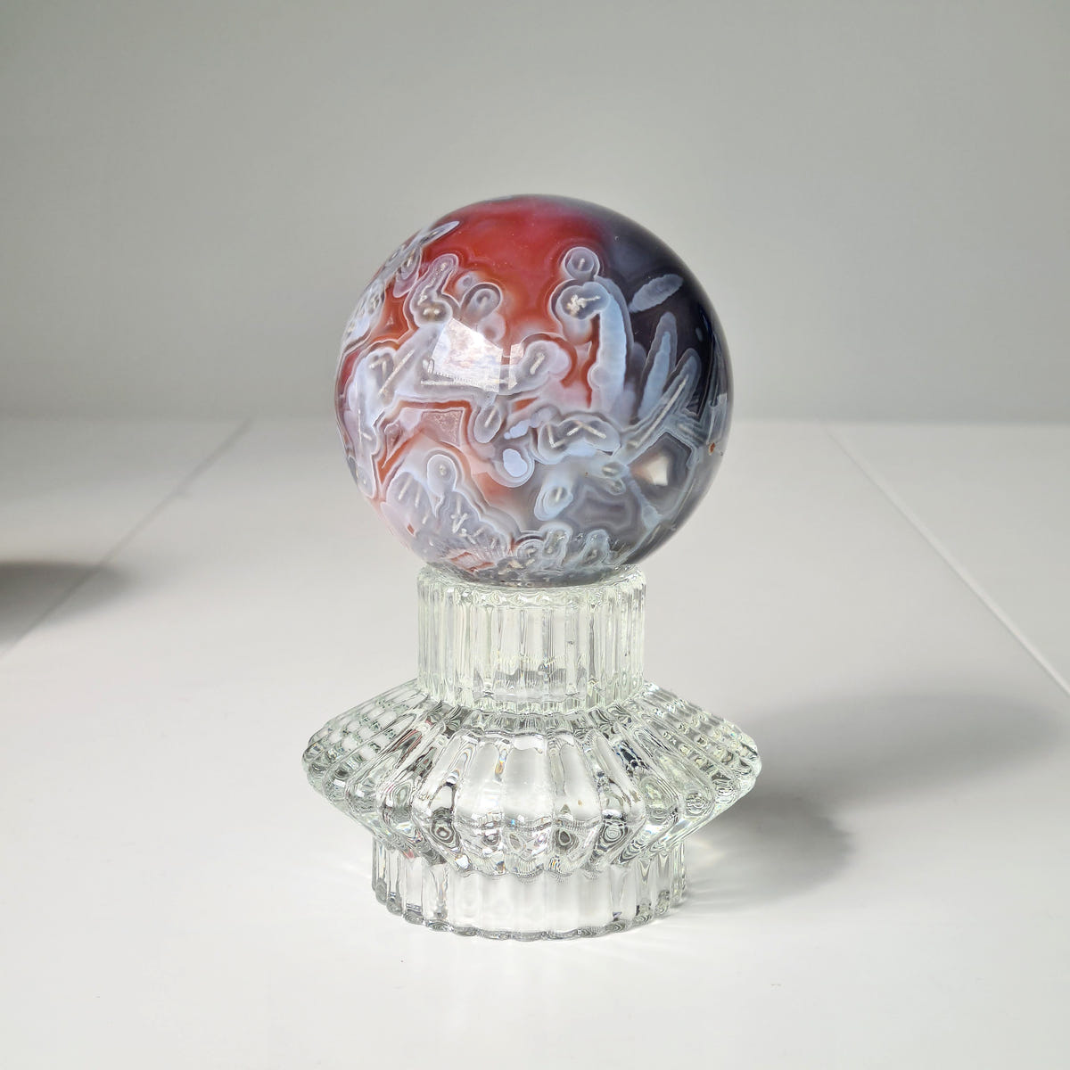 Swazi agate sphere A with red, grey and white swirling bands on a clear decorative stand.