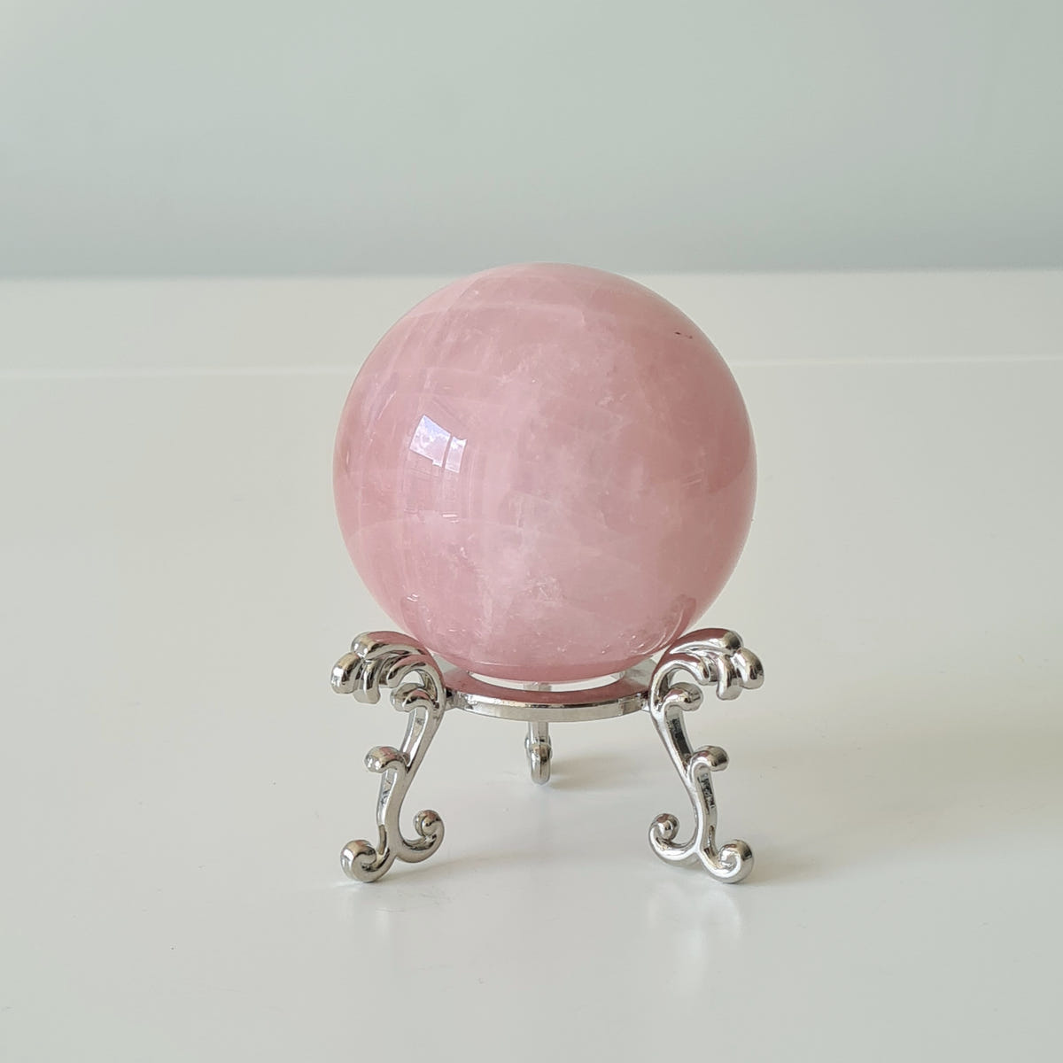 Polished pink rose quartz sphere displayed on a small silver-coloured ornamental stand.