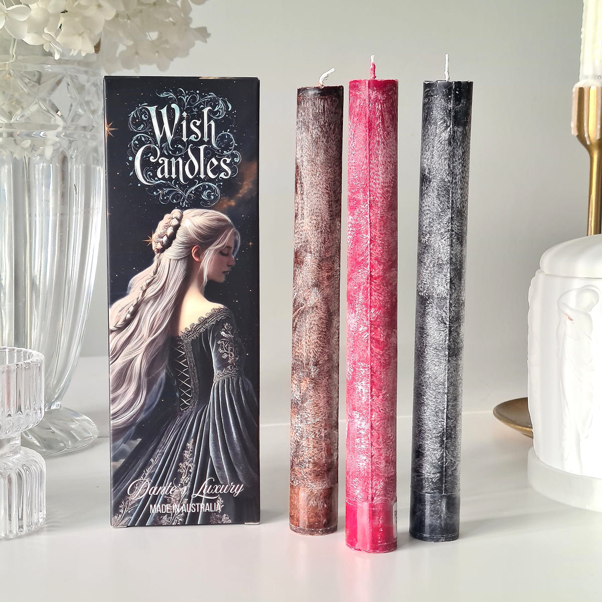 Strength and Manifestation wish-candle trio in brown, pink and black beside an illustrated box.