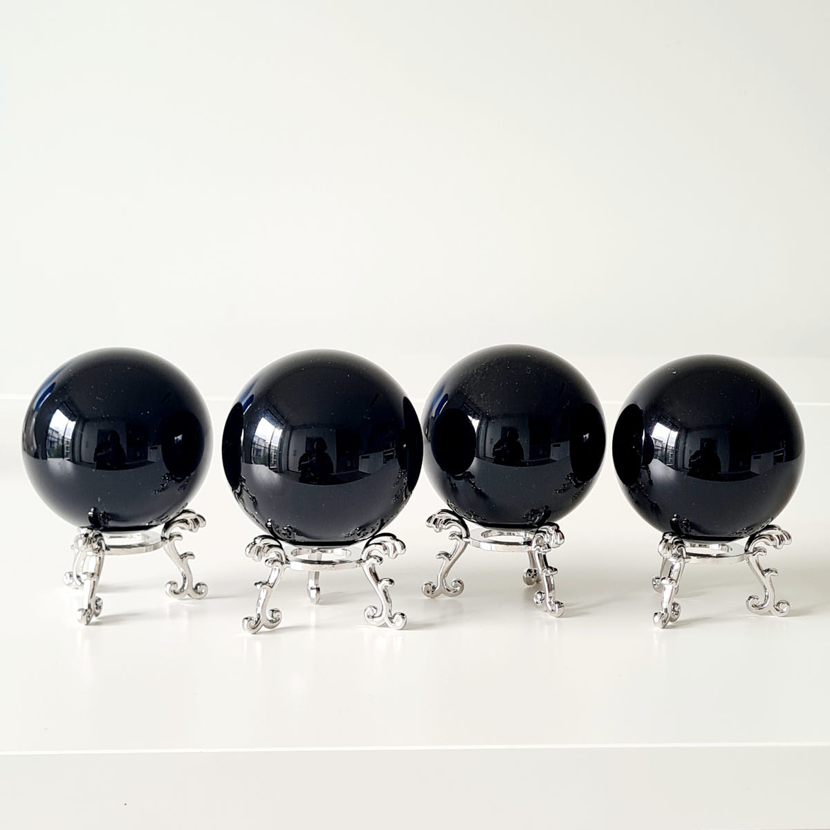 Four polished black obsidian spheres displayed on small silver-coloured ornamental stands.