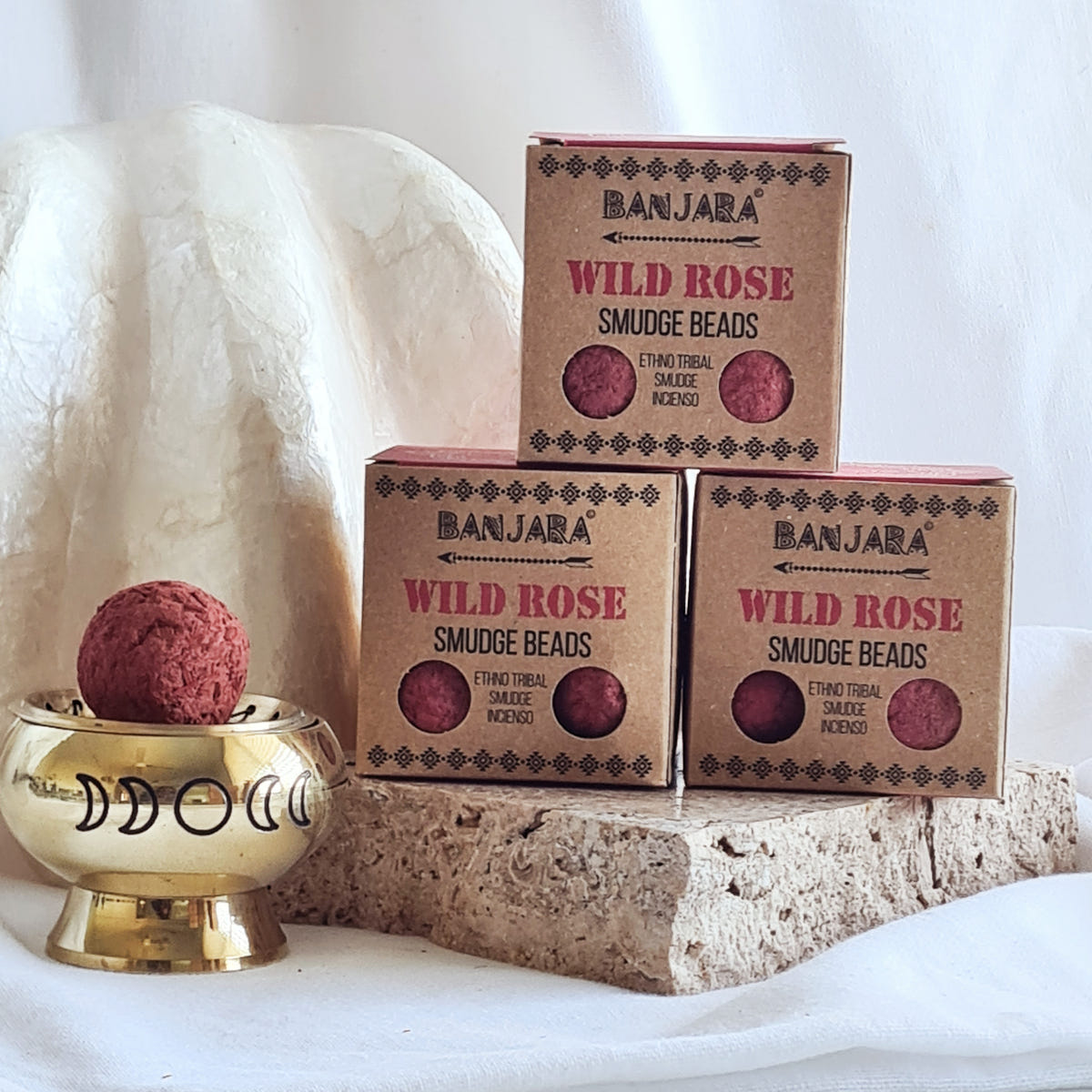 Three Banjara Wild Rose smudge bead boxes beside a brass moon-design burner holding a pink round bead.
