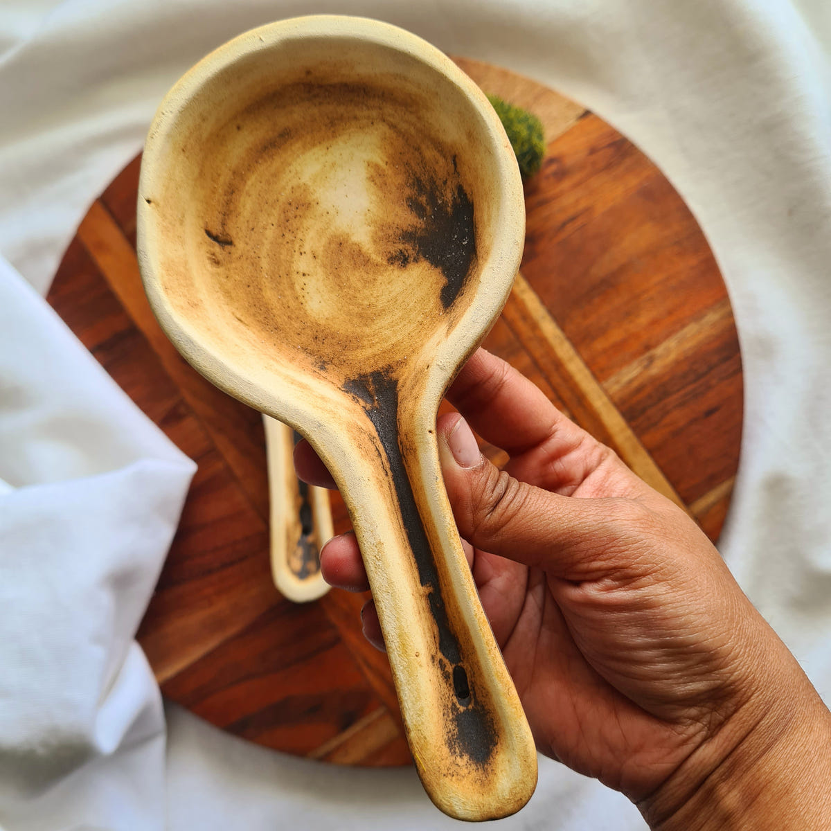 Hand holding a golden-brown ritual burner with a rounded bowl and a long handle.