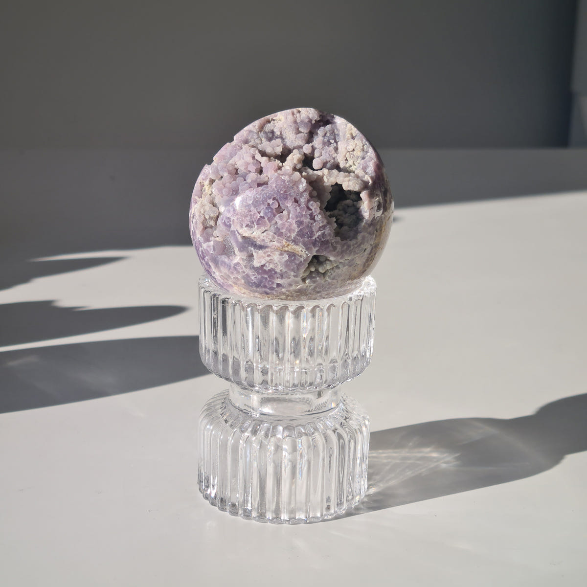 Grape agate sphere C with pale purple clustered formations and dark natural pockets on a clear ribbed stand.