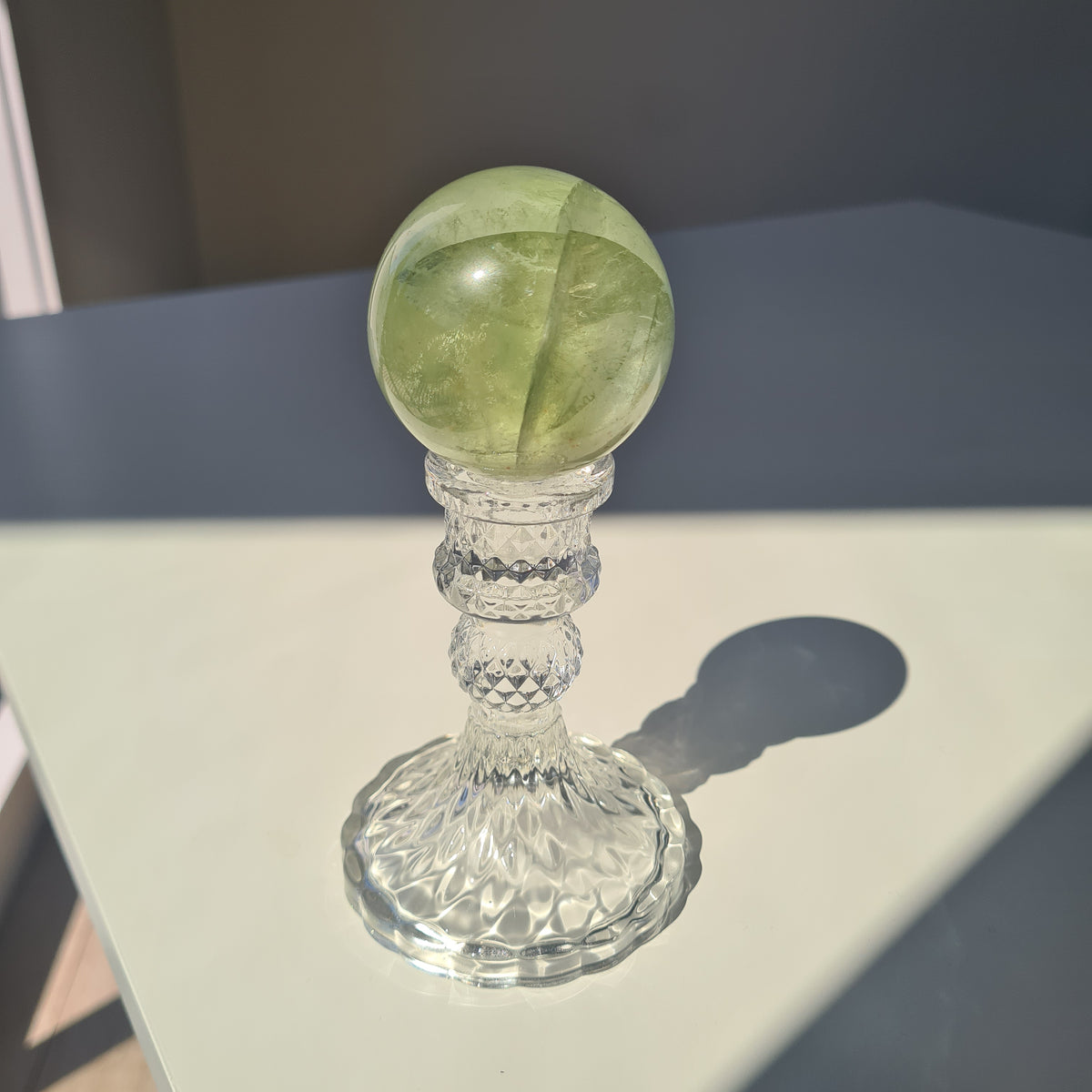 Golden-green fluorite sphere with translucent layers on a clear decorative stand.