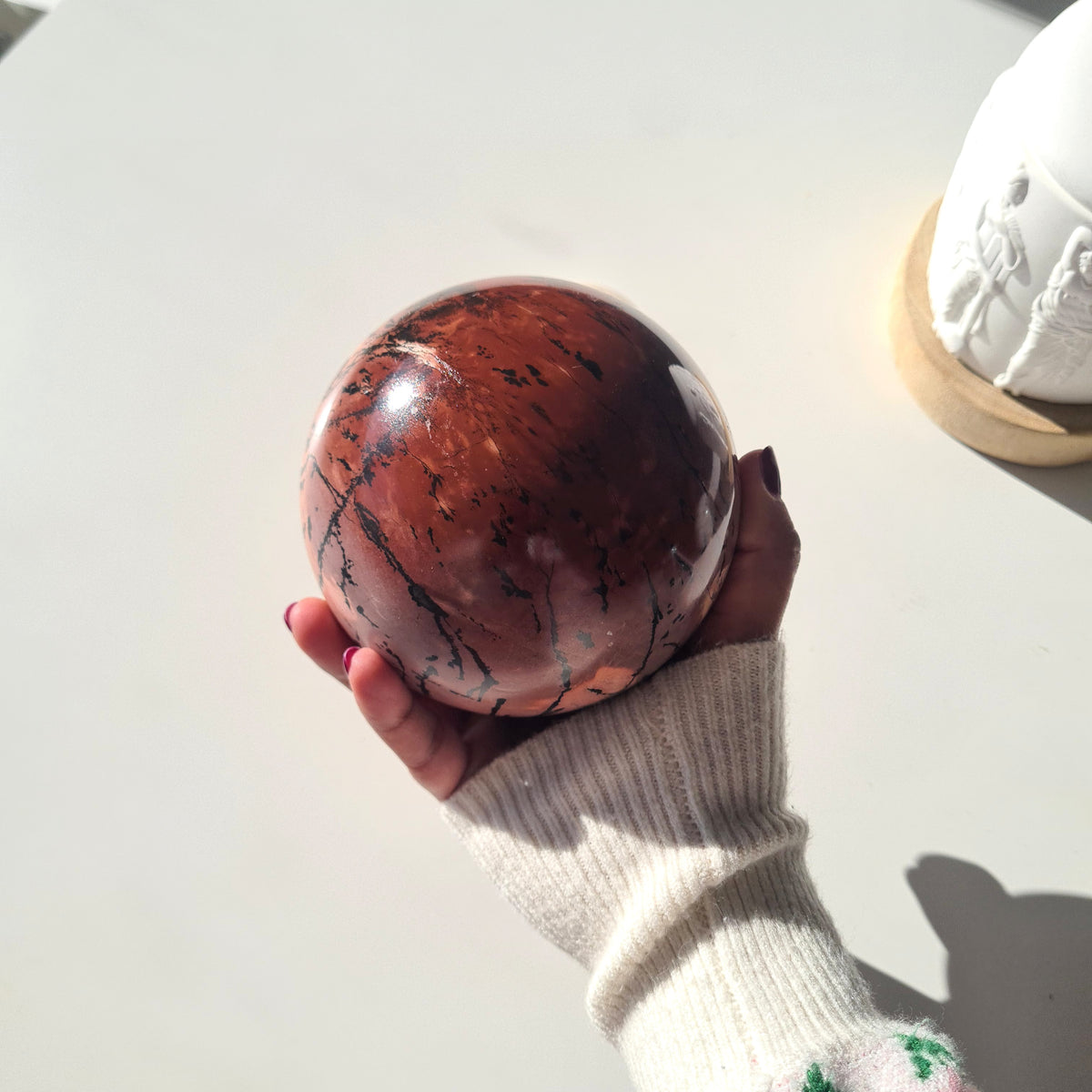 Picture jasper sphere held in one hand, showing its dark red side and fine black lines.